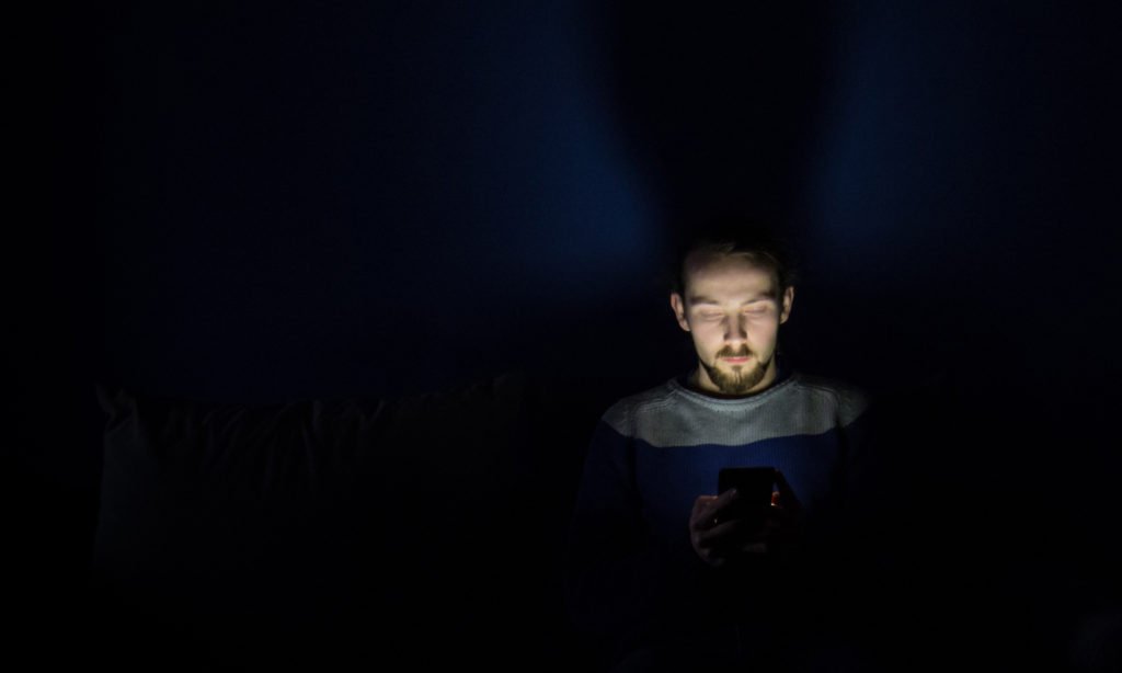 Man addicted to his cell phone, staring at the phone's bright screen while sitting in the dark